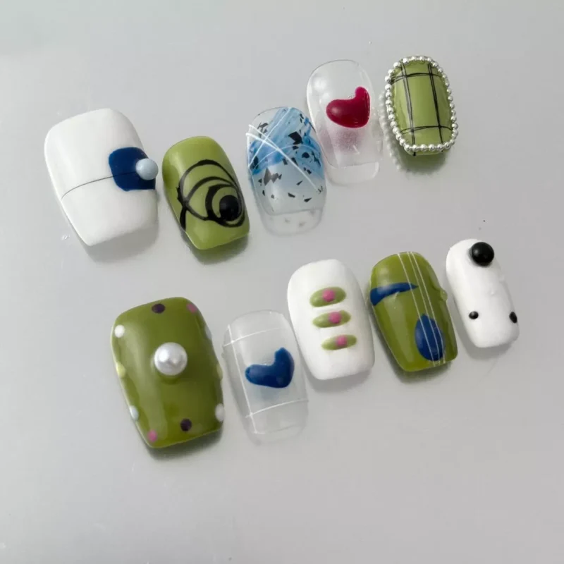 Close-up of olive green and white press-on nail with 3D heart and pearl charm accents