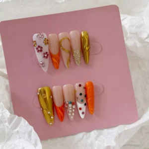 Orange press-on nails with 3D charms and chrome bead detailing – flat lay