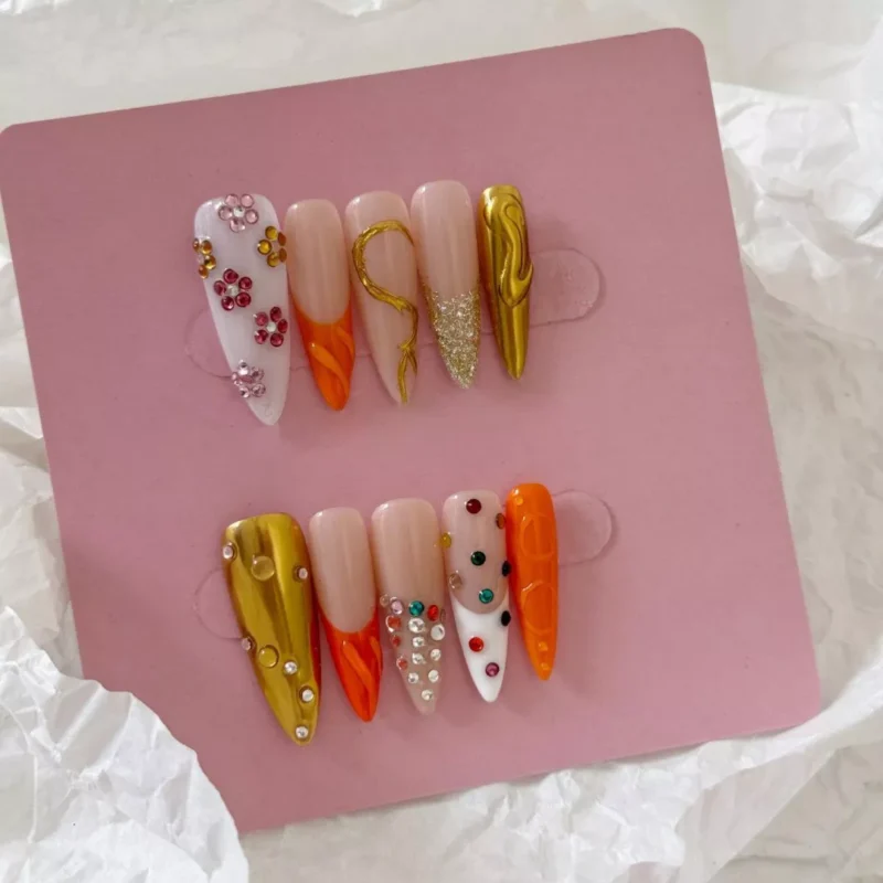 Orange press-on nails with 3D charms and chrome bead detailing – flat lay