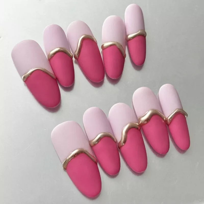 Close-up of almond-shaped pink matte press-on nails with gold wave accents