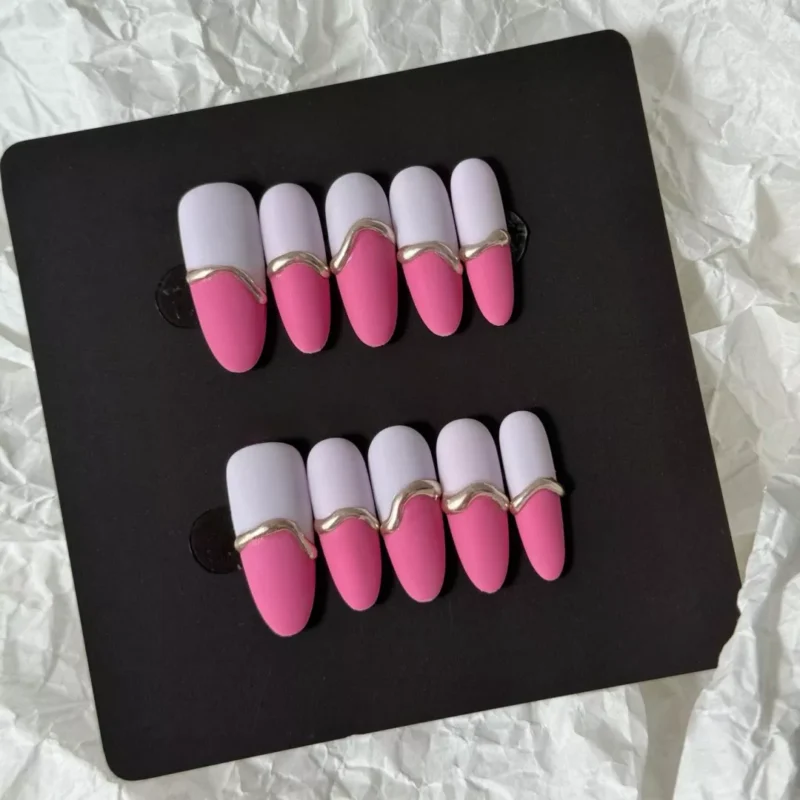 Pink matte press-on nails set featuring dual-tone pink and white base with artistic gold wave accents