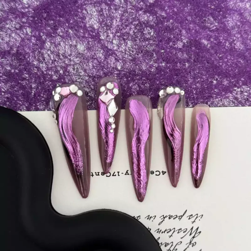 Long glossy stiletto nails with metallic pink art strokes and rhinestones