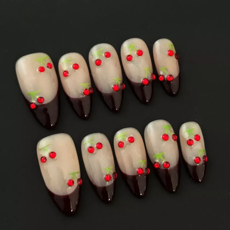 Detail view of cherry nail art with rhinestones on almond nude nails