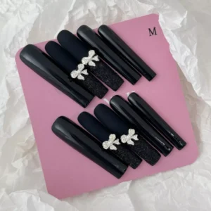 Styled display of black bow press-on nails with high-shine and matte sections – elegant setting