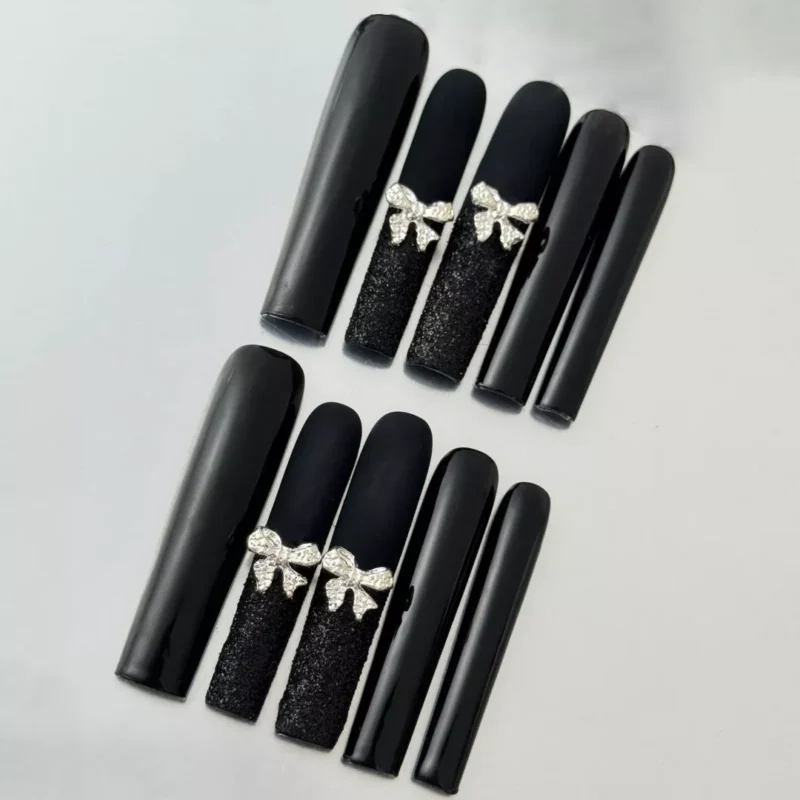 Close-up of glitter bow accent on long black matte press-on nail with square shape