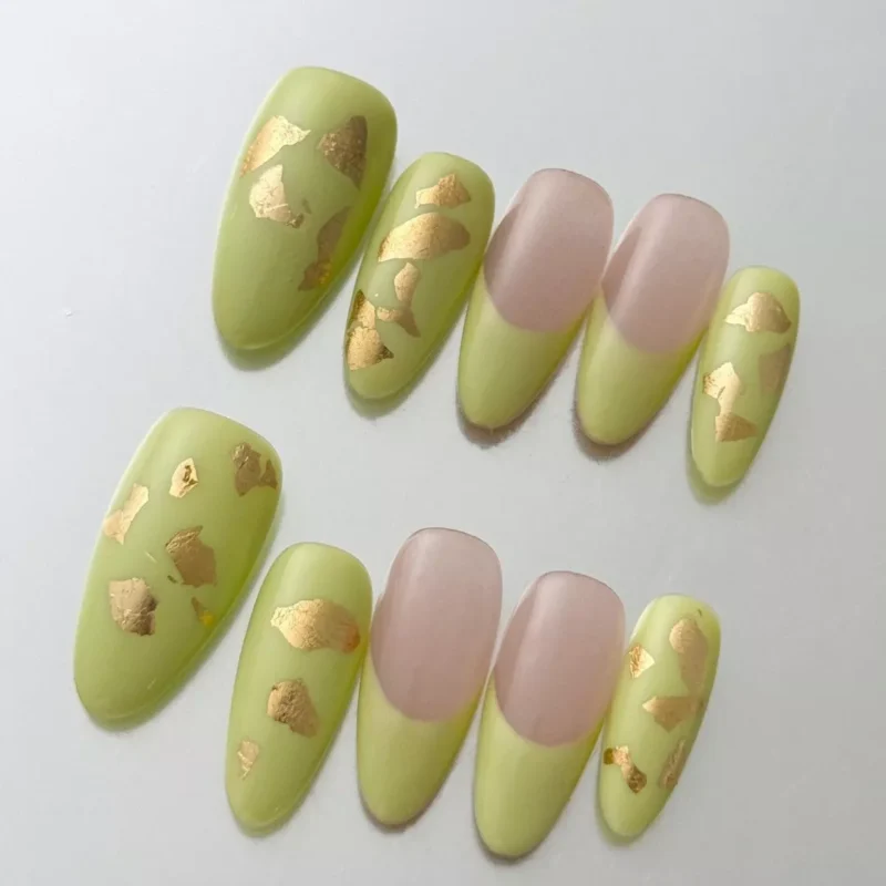 Close-up of almond-shaped green press-on nails with matte texture and metallic gold foil
