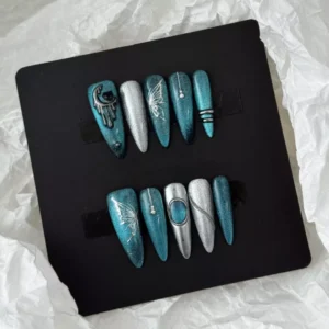 Styled display of teal glitter nails with gothic butterfly and moon metal charms