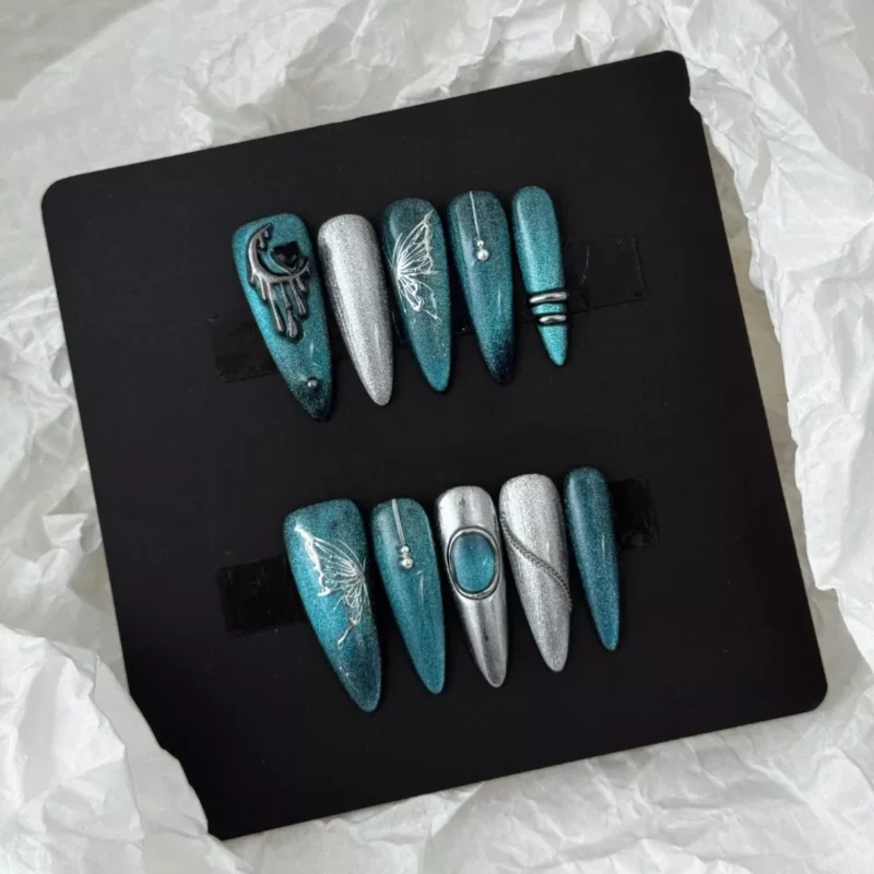 Styled display of teal glitter nails with gothic butterfly and moon metal charms