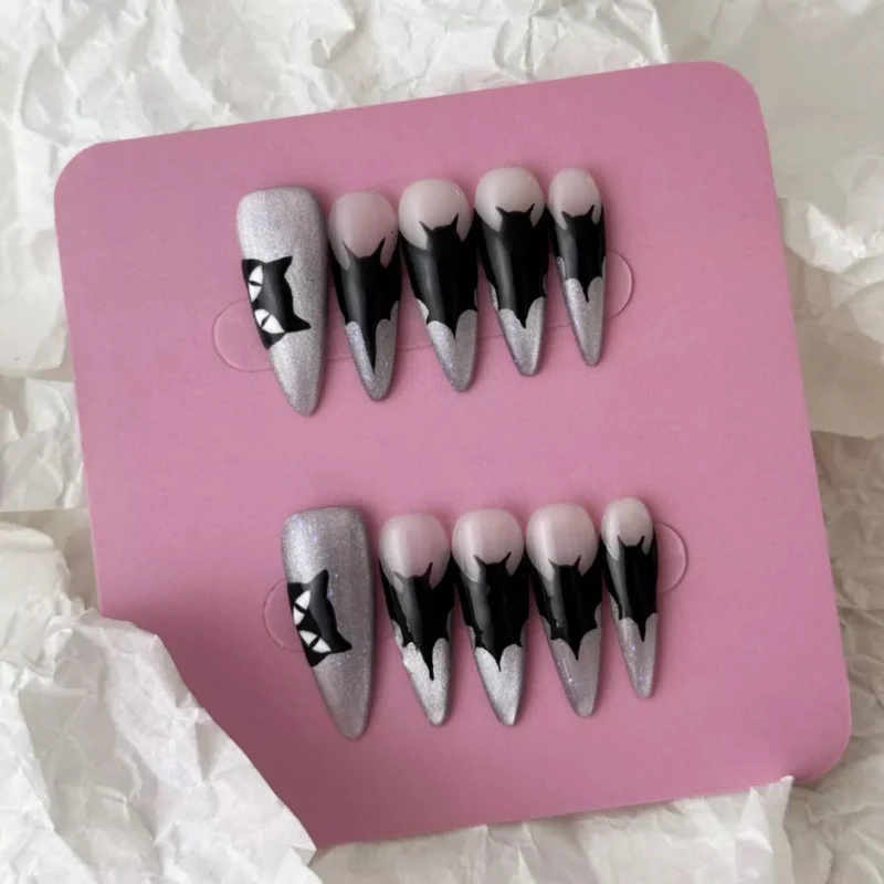 Flat lay of gothic press-on nails with black dripping tips and cat silhouette on glitter base
