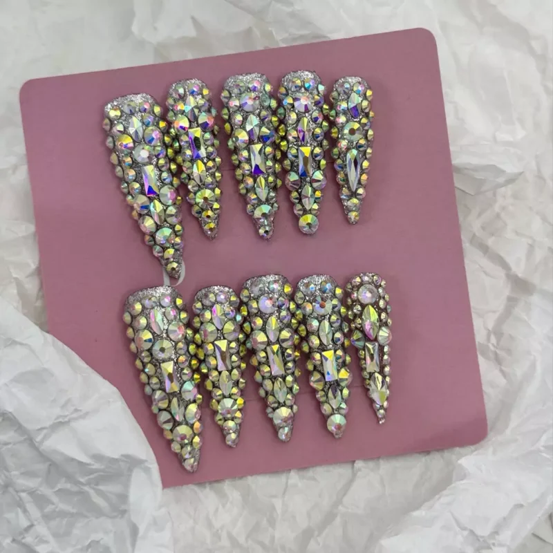 Full set of glitter rhinestone nails laid out on pink background