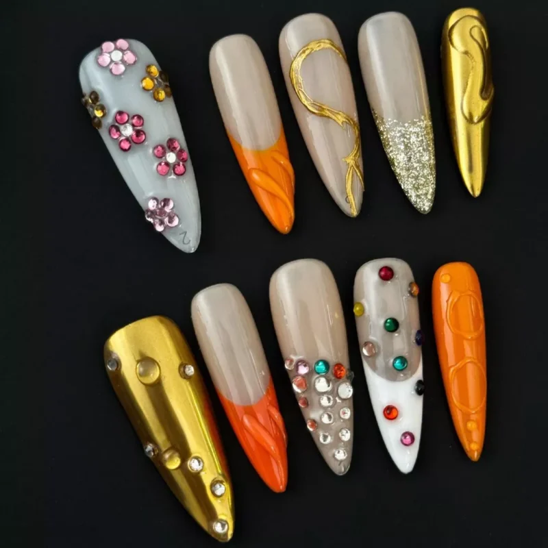 Side angle of mixed orange nails showing texture and layered embellishment