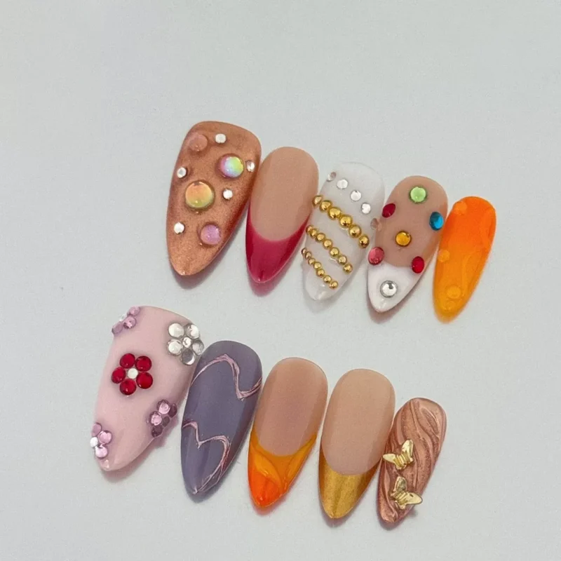 Nude and orange press-on nails with butterfly gold tips and 3D accents
