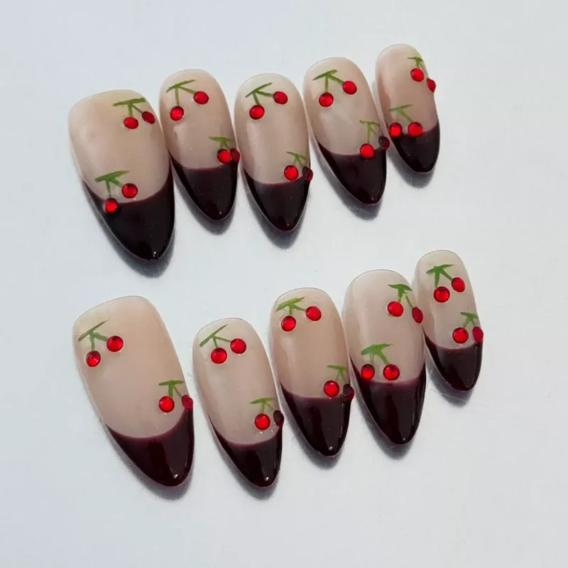 Side angle of nude press-on nails with glossy red V-tip and cherry rhinestone accent