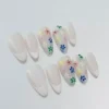 Oval-shaped nude press-on nails with pastel flower embellishments and glossy finish