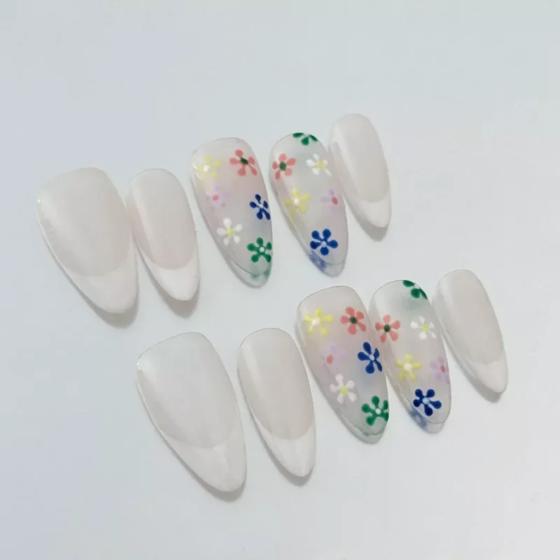 Oval-shaped nude press-on nails with pastel flower embellishments and glossy finish