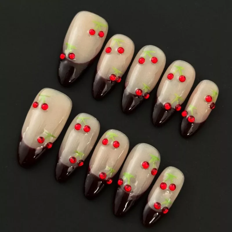 Close-up of Rhinestone Cherry Press-On Nails with nude base and dark red V-tips featuring cherry gem design