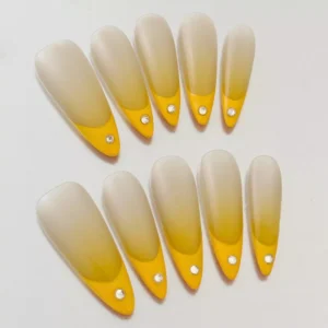 Sheer nude ombre nails with yellow French tips and gem highlights – close-up