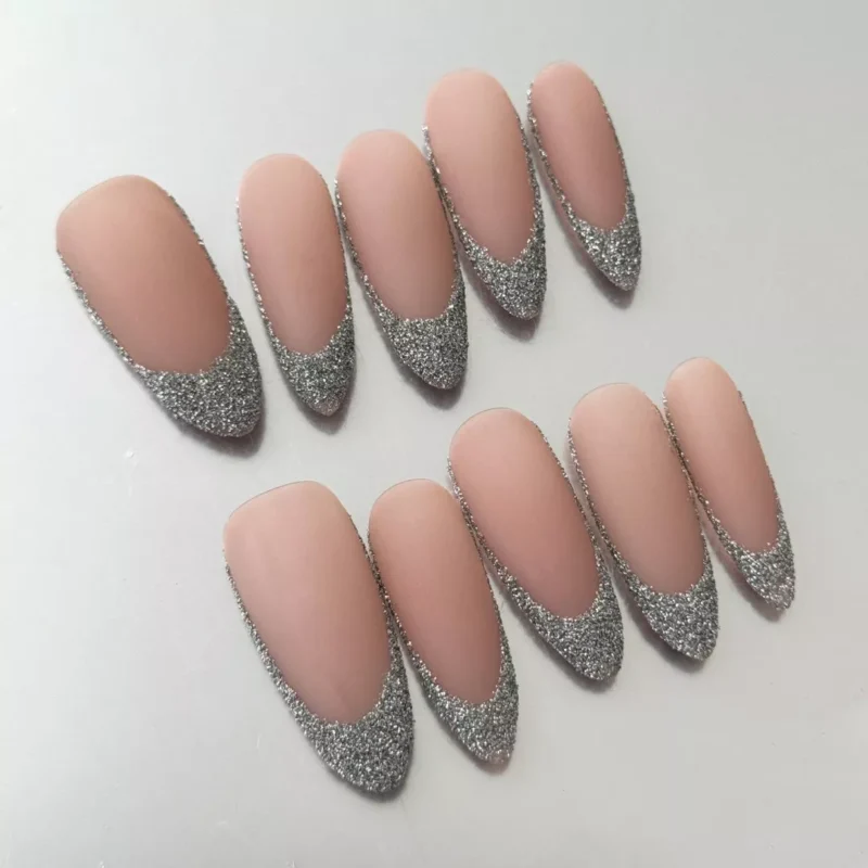 Close-up of silver French tip on matte nude almond press-on nail with textured glitter