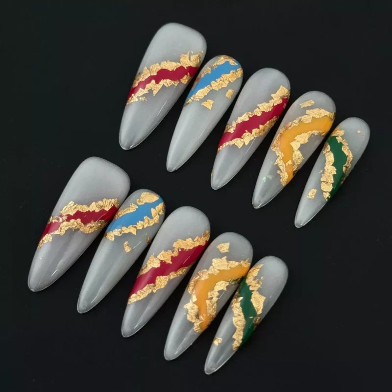 Abstract gold foil press-on nails with red and blue streaks on sheer stiletto base – side view