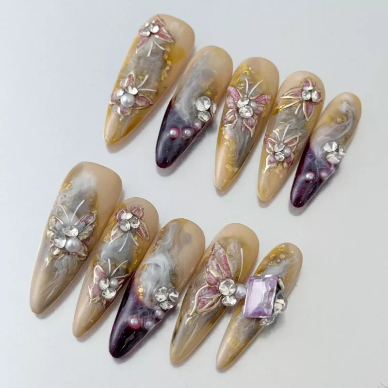 Oval beige press-on nails featuring rhinestones, pearl beads, and layered flower accents – close-up