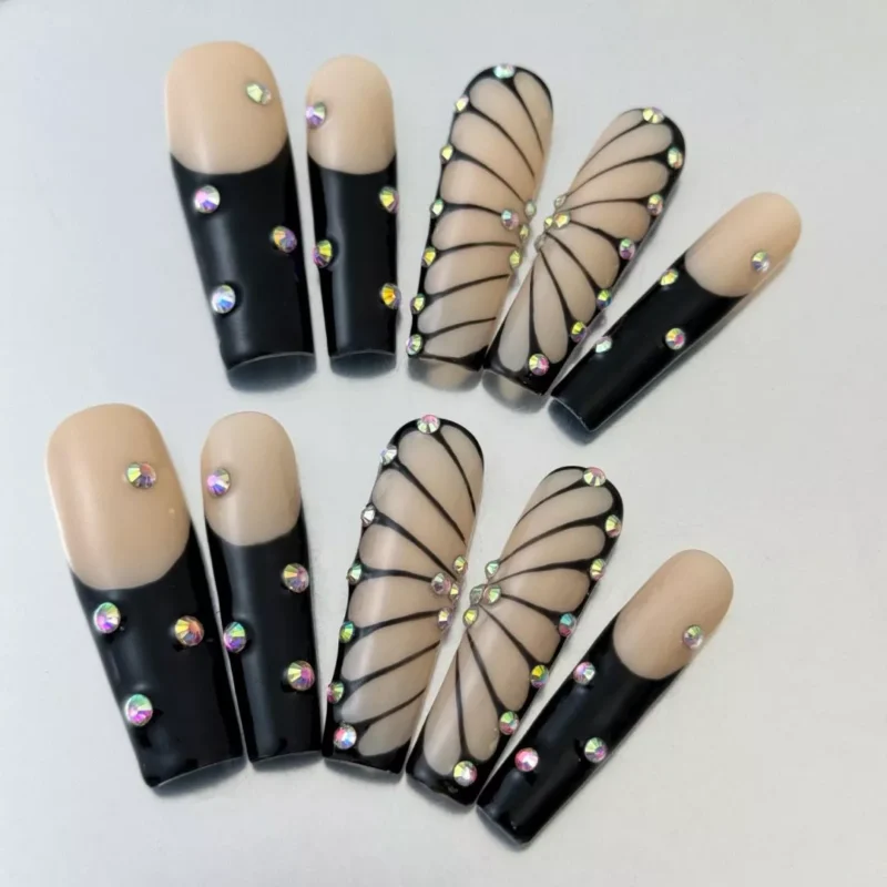Glossy nude press-on nails with butterfly rhinestones and artistic black strokes – side perspective
