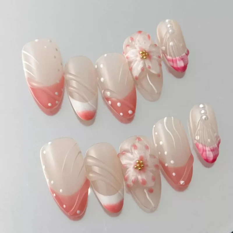 Close-up of almond-shaped press-on nail with 3D sakura blossom and gold bead center