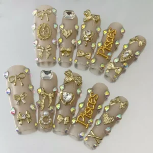 Close-up of 3D gold bow nails with sacred heart accent on nude coffin tips