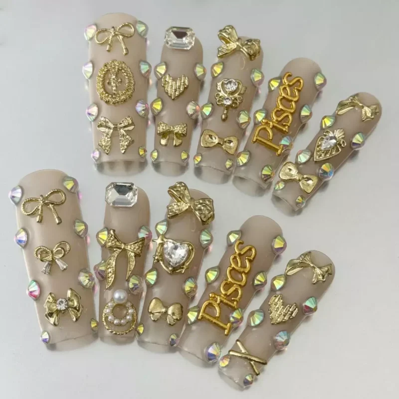 Close-up of 3D gold bow nails with sacred heart accent on nude coffin tips