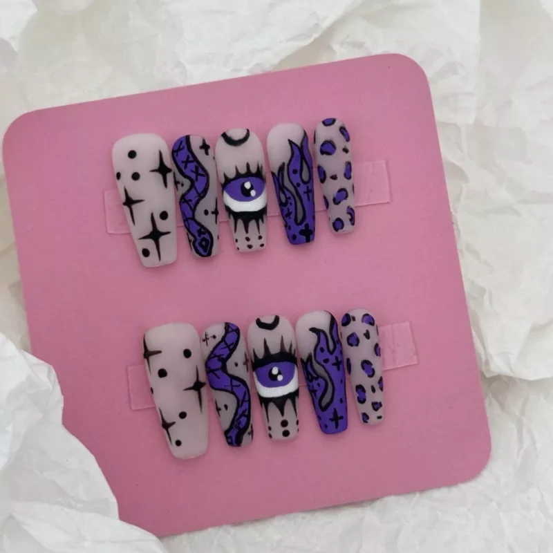Hand-drawn Gothic nails with flame, eye, and moon symbols in purple ink on matte base