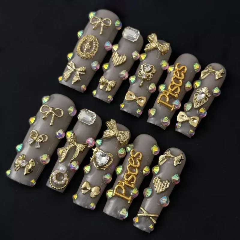 Nude rhinestone press-on nails with 3D gold bows and Pisces zodiac charms – top view