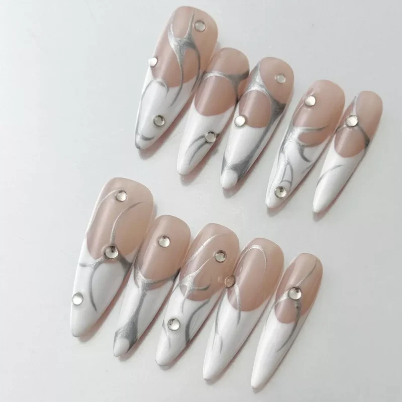 Close-up of long stiletto nude nails with abstract silver line art and rhinestone embellishment