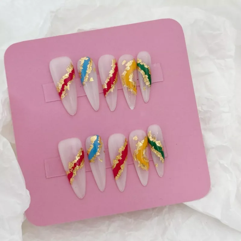 Abstract gold foil press-on nails displayed on pink tray with multicolor accents