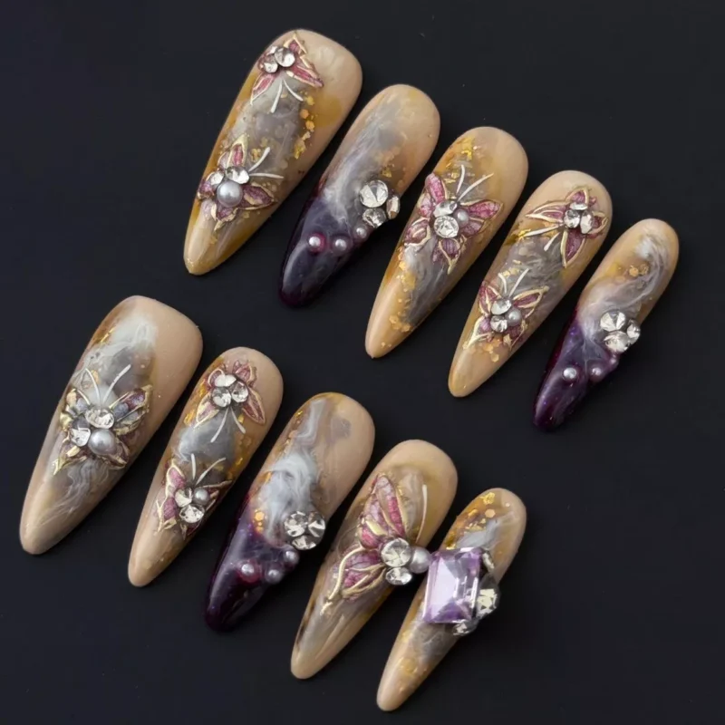 Smoky marble press-on nails in beige with 3D floral details and gold flake accents – angled front view