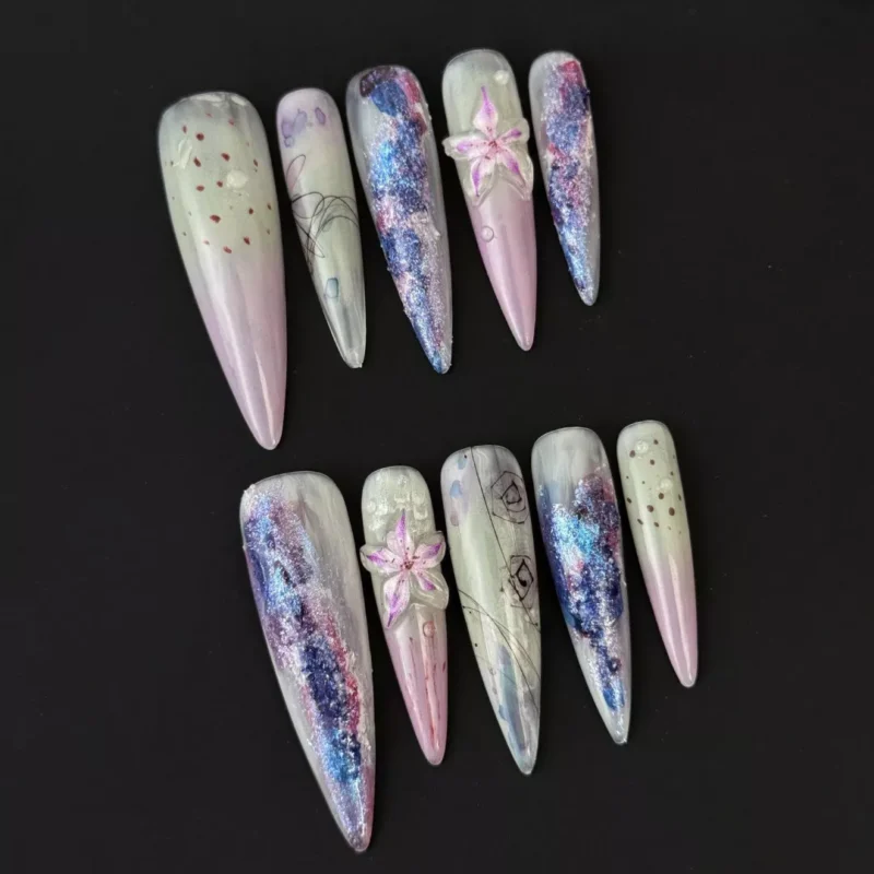 Side angle of long stiletto press-on nails in purple icy tones with embedded lily accents