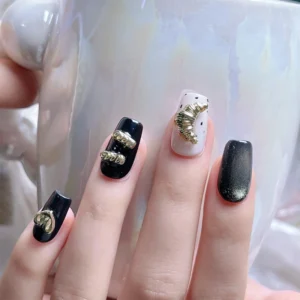 Manicure with gold metal heart and bar charms on black nails holding an iridescent mug
