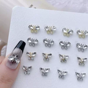 Close-up of silver and gold crystal butterfly nail charms arranged on white board