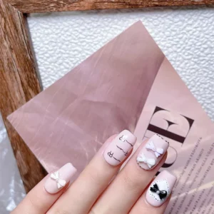 Stylized hand pose with nude nail base and pastel pearl bow nail charms on fingertips
