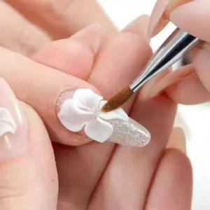 Nail artist sculpting white 3D flower on clear gel base using fine brush