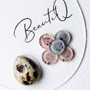 Macro of speckled gel polish samples styled next to natural quail egg