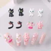 Girly cartoon nail charms in black cat, white dog, and pink bunny designs displayed with sample nail tips