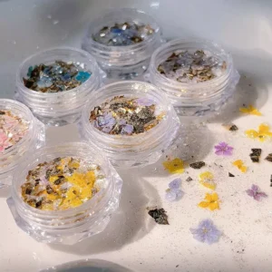 Gold foil and floral glitter spilling from jars onto white background