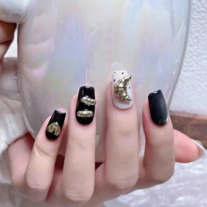 Close-up on four fingers with gold moon and bar nail charms on different polish styles
