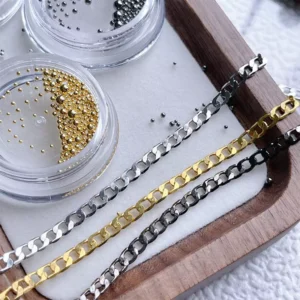 Gold, silver, and black nail chains aligned beside microbeads on white tray