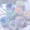 Assorted pastel iridescent pebble nail charms in round containers
