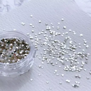 Silver heart nail glitter sequins spilled beside clear container