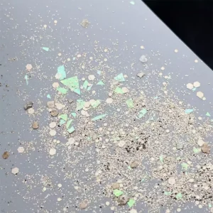 Iridescent green and gold hex glitter flakes on neutral surface