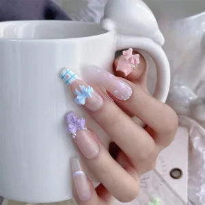 Close-up of pastel bow nail decorations applied to long acrylic nails holding a ceramic mug