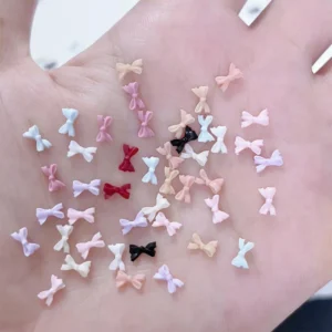 Matte and glossy mini resin bow nail charms in pastel and nude tones spread on hand