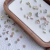 Mixed metal nail charms in heart, moon, and grid shapes on a tray, gold and silver finishes