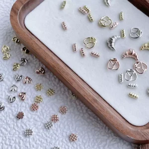 Mixed metal nail charms in heart, moon, and grid shapes on a tray, gold and silver finishes
